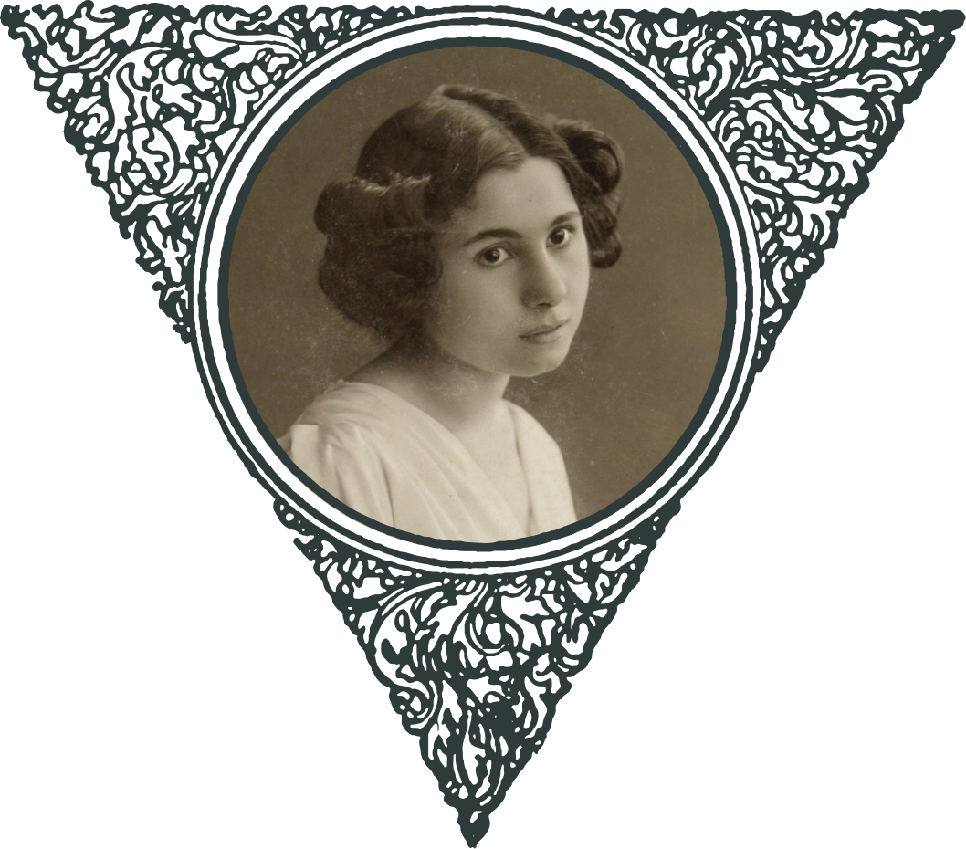 Ein historisches Schwarz-Weiß-Porträt einer jungen Frau mit lockigem Haar und einer Blume an ihrer Schulter. Unten auf dem Foto steht "Marie Mertens - Photograph-Kunst-Atelier 'Moderne' in Wien."
